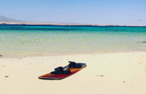 A kiteboard lying on an empty beach in front of the glassy turquoise sea