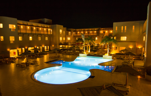 The Breakers Diving & Surfing Lodge at night, featuring a beautifully illuminated pool and a relaxed atmosphere.