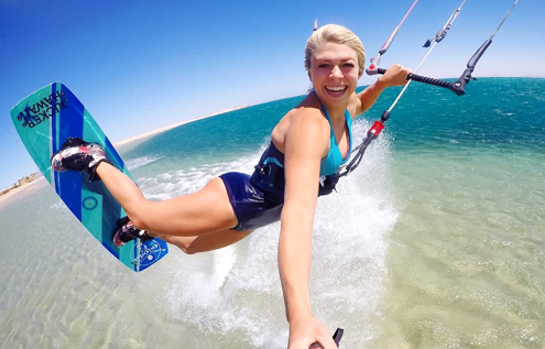 Smiling female kitesurfer jumping over crystal-clear water in Somabay, Egypt.