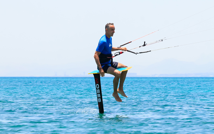 Kite foiler in a blue wetsuit gliding above the water on a Moses hydrofoil board in Soma Bay.