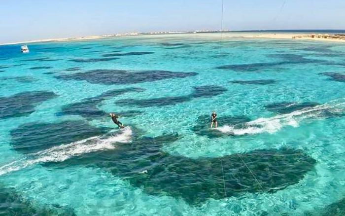Two kitesurfers gliding over turquoise waters and coral reefs near KiteHouse Somabay