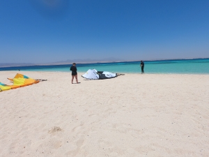 Kitesurfers preparing their gear on the sandy beach of Soma Bay, with turquoise waters and a clear blue sky in the background.