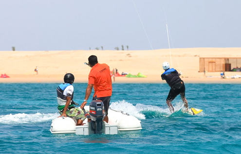 Ein Kitesurf-Schüler fährt übers Wasser, während ein Instructor vom Begleitboot aus Anweisungen gibt. Perfekte Bedingungen für sicheres und effizientes Lernen im KiteHouse Somabay.