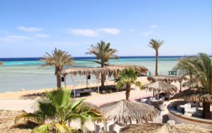 Beachfront view at The Breakers, Soma Bay, with palm trees, shaded seating, and turquoise waters.